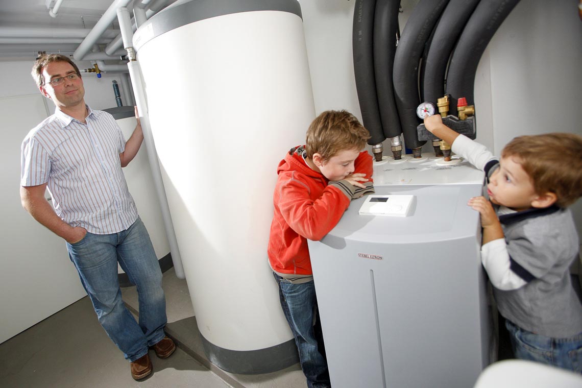 Wenn die Eltern auf die Wärmepumpe setzen freut sich der Nachwuchs: Um Bild steht lehnt der Vater an die neue Technik, während Kinder die Zähler ablesen.