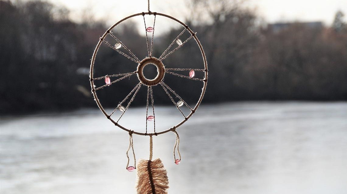 Traumfänger wird vor eine Seenlandschaft gehalten.