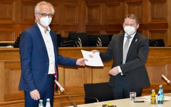 Bildunterschrift: Der hessische Minister für Wirtschaft, Ernergie, Verkehr und Wohnen Tarek Al-Wazir (links) überreicht dem Präsidenten von Hessen Mobil Prof. Gerd Riegelhuth die Abschiedsurkunde. Foto: Hessen Mobil