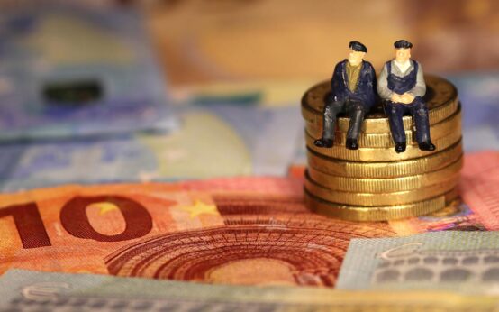 Zwei Renter sitzen auf einem Berg 50 Cent Münzen, umgeben von Euro Scheinen