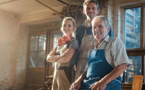 Nachfolge: Generations of carpenters in their family business workshop looking at the camera
