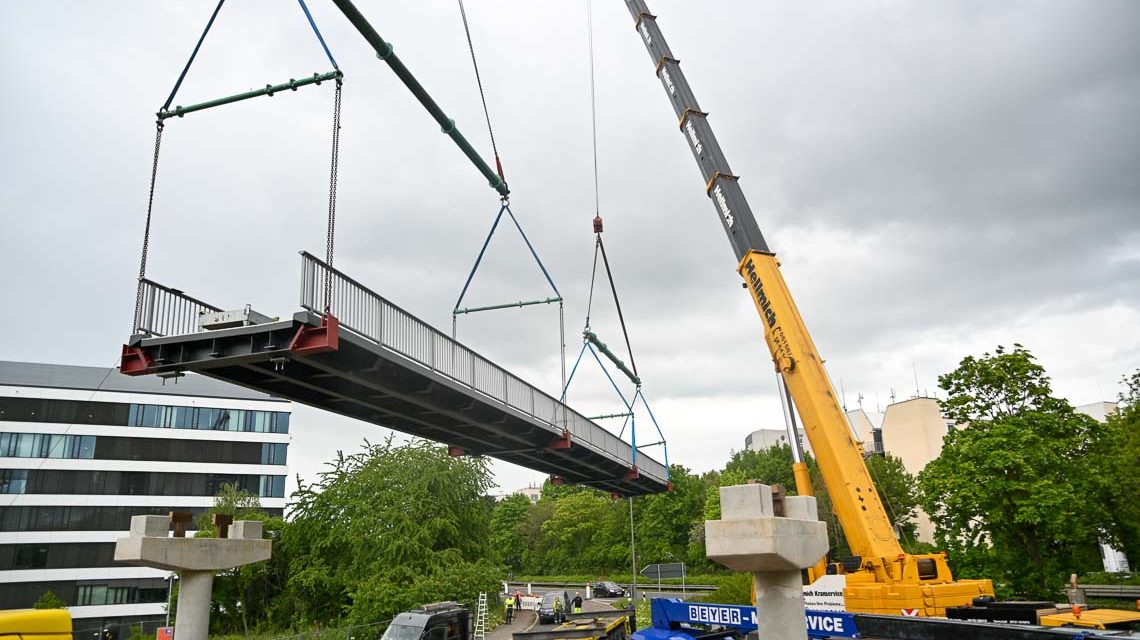 Fußgängerbrücke verbindet die Bushaltestelle Siegfriedring südlich der Berliner Straße mit dem nördlich liegenden Gebiet (Abraham-Lincoln-Straße). Im Bild schwebt sie gehalten von zwei Krahnwagen ein.