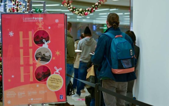 Impfzentren: Luisenforum. Schlange stehen zum Impfen. Morgens um 9:00 Uhr stehen die ersten an, reihen sich ein, erhalten den Anamesebogen auf der Straße und werden aufgeklärt, welche Dokumente notwendig sind: Personalausweis und Krankenkarte + Impfausweis.