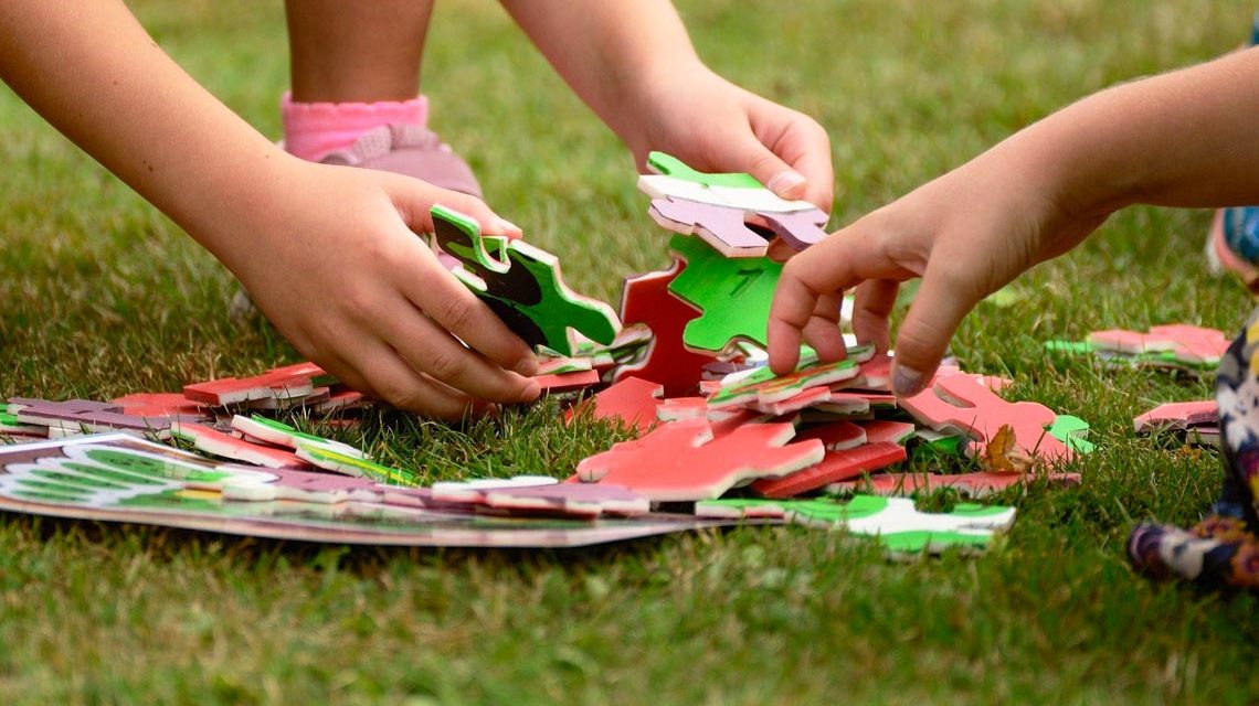 Kinderhände puzzeln auf einer grünen Wiesse.
