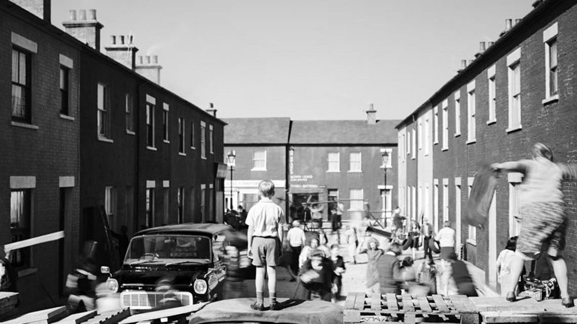 Kleiner Junge steht auf einem Autodach und beobachtet einen Aufruhr.