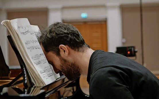 Igor-Levit sitzt am Klavier und vergräbt seinen Kopf in Noten.