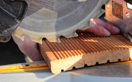 Schreiner, Bodenverleger bei der Arbeit. Das Bis zeigt eine Kreissäge und jemanden, der Bodendielen kürzt.