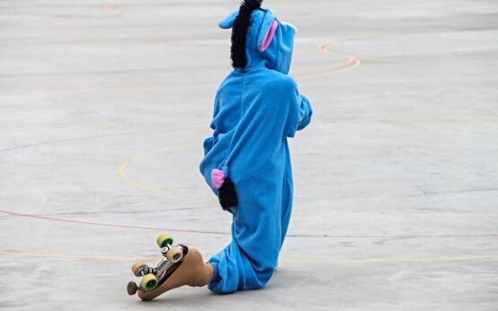 Rollschuhlaufen, Rollschuhläufer kostümiert auf der Bahn kniend.