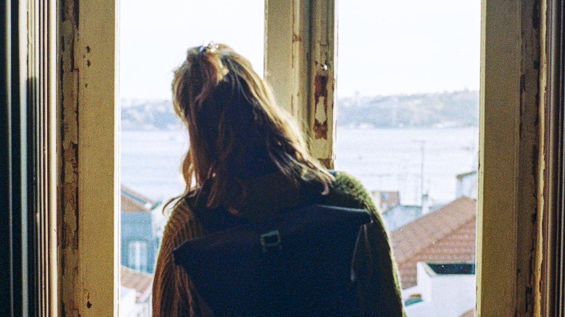 Frau schaut aus dem Fenster einer Sozialwohnung.