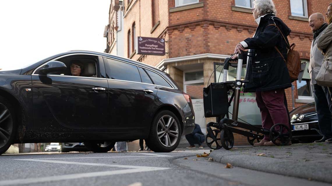 Frau mit Rollator versucht über die Straße zu gehen.