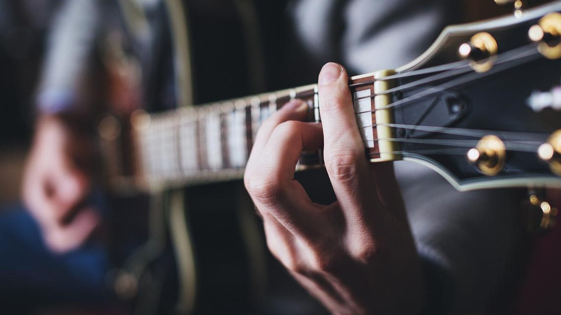 Gitarrenspieler, das Bild zeigt eine Gitarre groß, mit den Händen am Riff.