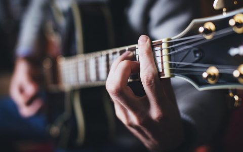 Gitarrenspieler, das Bild zeigt eine Gitarre groß, mit den Händen am Riff.