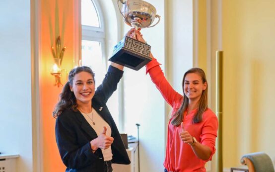 Die Wiesbadenerin Kim Kalicki und die Kölnerin Leonie Fiebig, Weltmeisterin im Zweiter-Bob strecken den Pokal empor.
