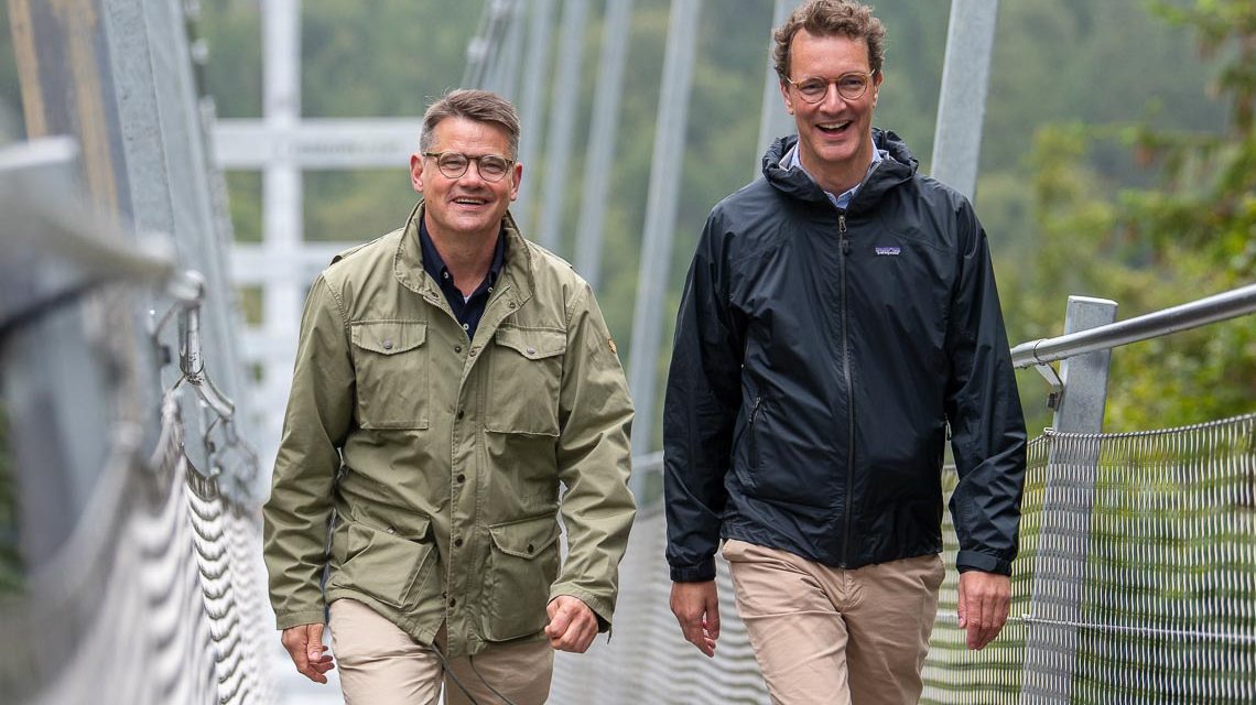 Ministerpräsidenten Rhein und Wüst gehen über Hängebrücke.