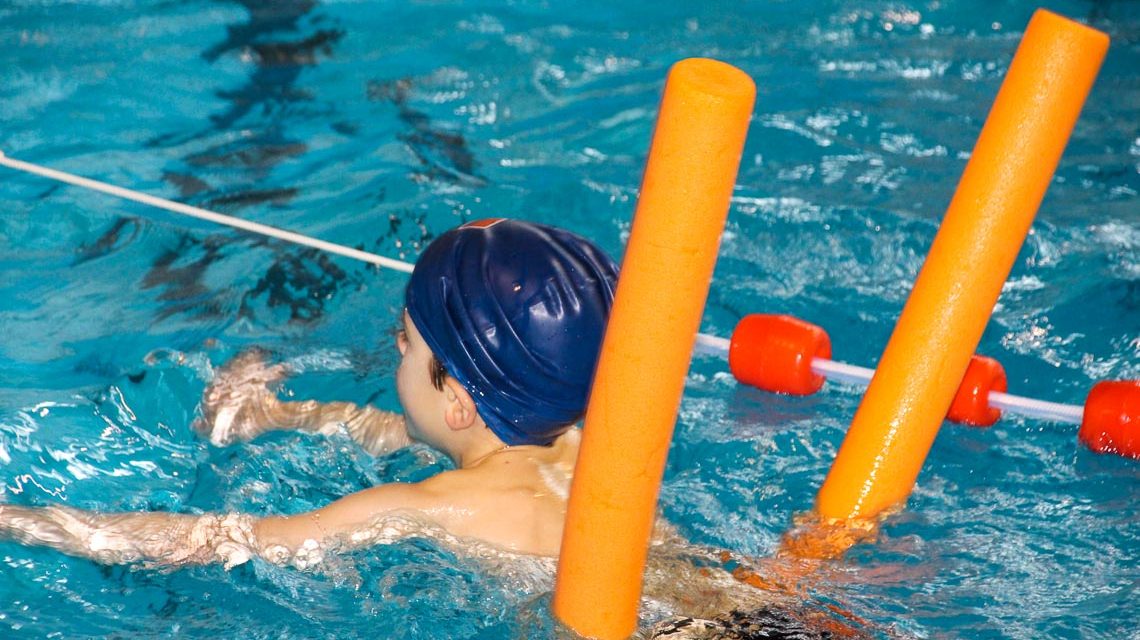 Schwimmkurs, kleiner Junge schwimmt mit Schwimmnudel.