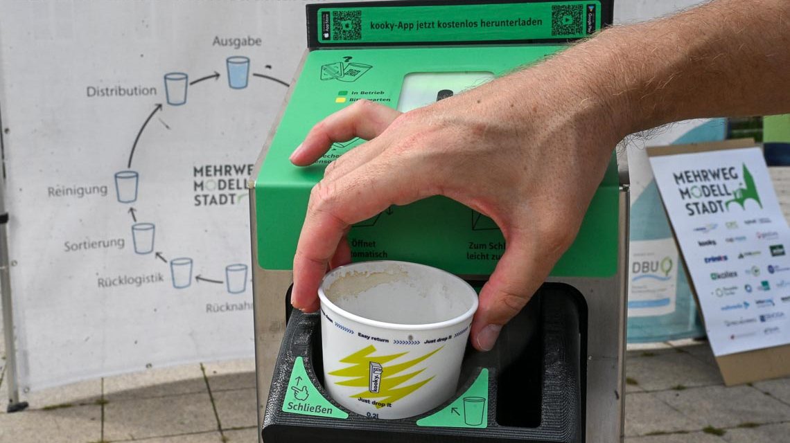 Reusable To-Go: Hand gibt Becher in einen Becher-Rücknahme-Automaten.