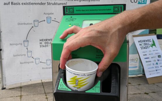 Reusable To-Go: Hand gibt Becher in einen Becher-Rücknahme-Automaten.