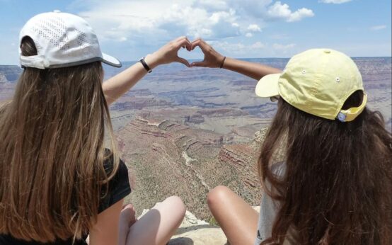 Zwei Schüler sitzen irgendwo in den USA auf einen Felsen und blicken in die Ferne. Mit den Händen formen sie ein Herz: Auf in die Welt-Messe!