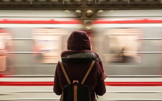 Reisende an einem Bahnsteig stehend und Zug fährt durch.