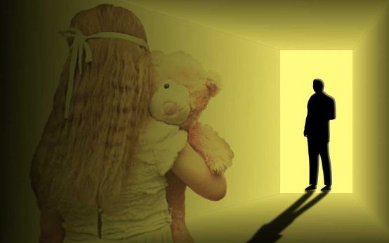 Mädchen mit Teddybär im Arm schaut zur Tür, wo ein Erwachsener steht.