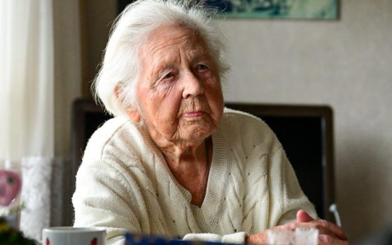 Gisela Voje, 103 sitzt in ihrem Wohnzimmer am Tisch.