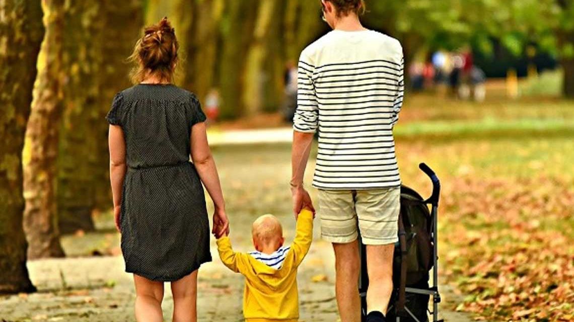 Junge Familie geht mit Kind durch den Park. Kinder betreuen, Angebhörige pflegen, Teilzeitbeschäftigung. Pflegeeltern