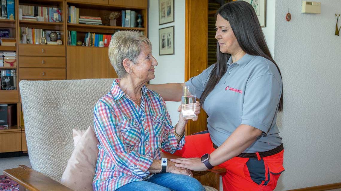 Hausnotruf: Rettungssanitäter der Johanniter reicht Frau ein Glas Wasser.