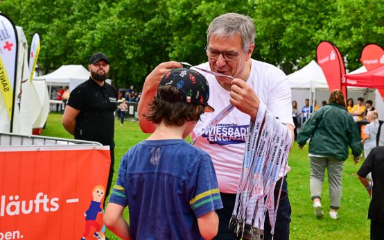 Gert Uwe Mende im Dienste von Wiesbaden engagiert hängt einem Schüler eine Medaille um.