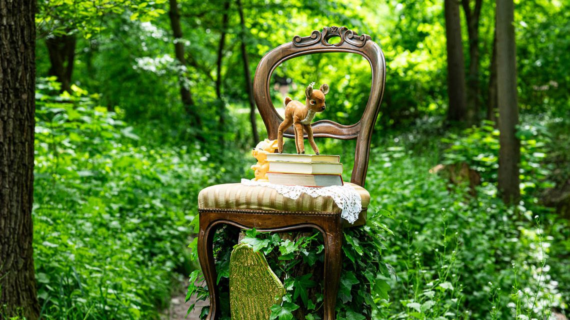 Ein gepolsterter Stuhl im Wald mit Büchern darauf nd einem Rehkitz.