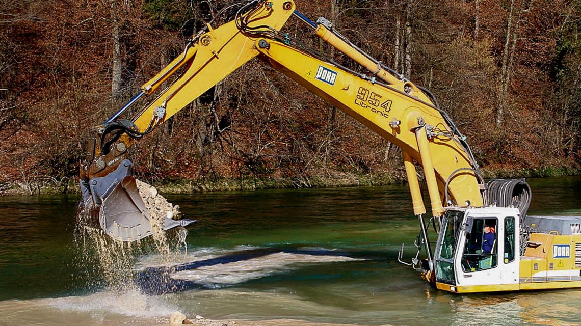 Bagger steht im Wasser und baggert Flussbett aus.