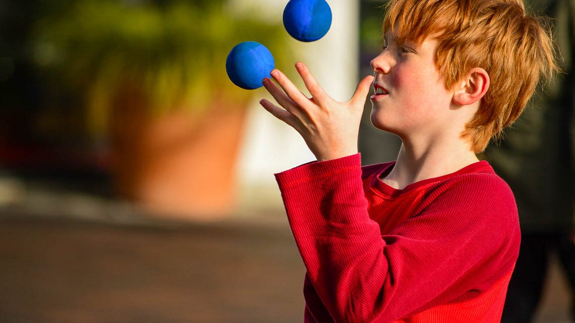 Junge jongliert mit zwei Bällen und über für den Kinderzirkus.
