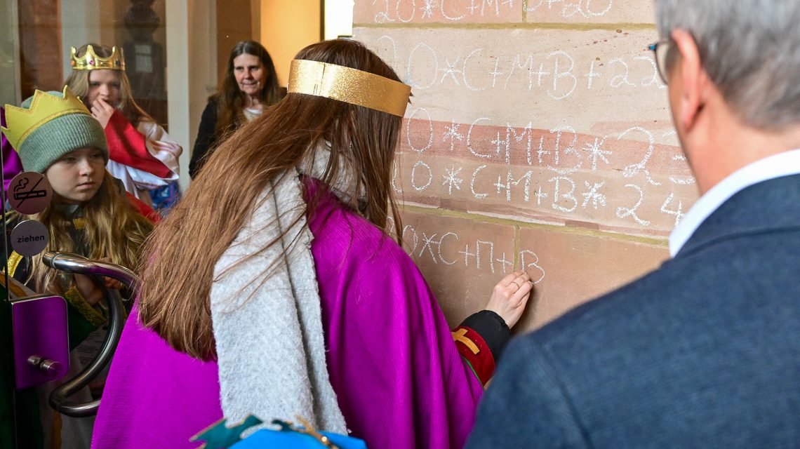 Sternsinger bringen Segen an der Pforte zum Rathaus an.