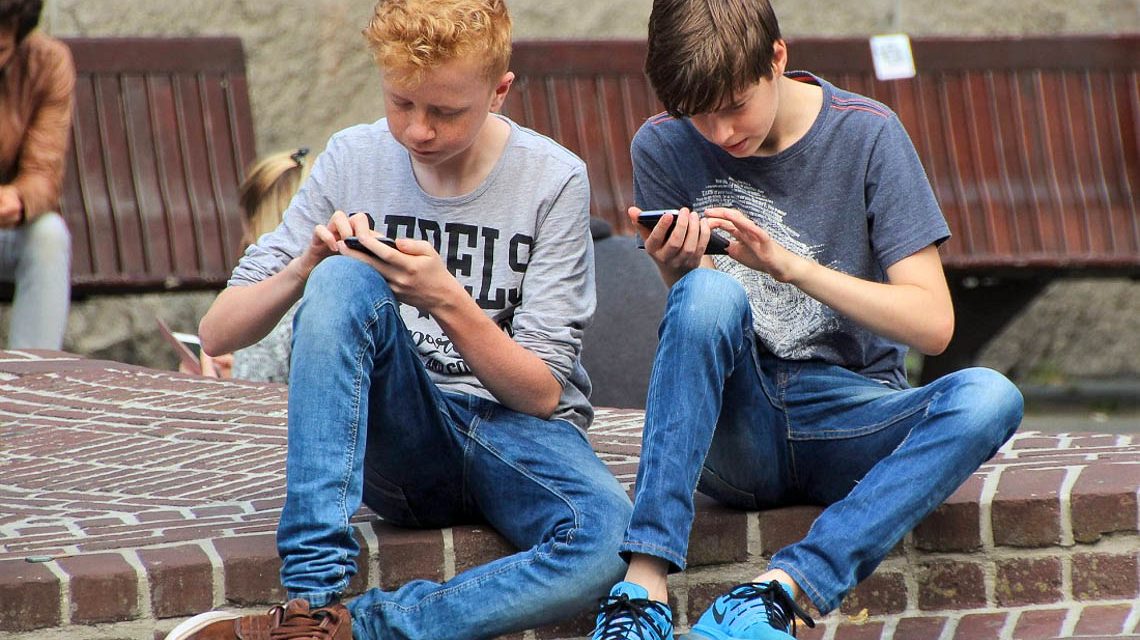 Zwei Schüler sitzen auf dem Schulhof und Datteln an ihrem Handy. Kommunikation ein Fremdwort.