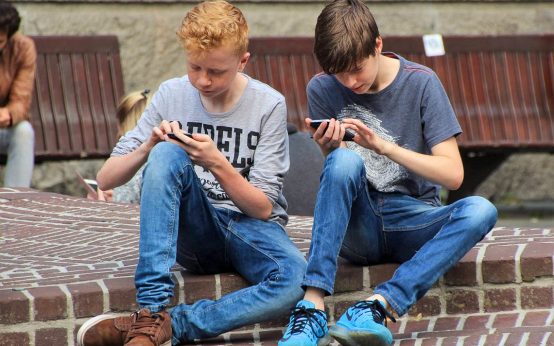 Zwei Schüler sitzen auf dem Schulhof und Datteln an ihrem Handy. Kommunikation ein Fremdwort.
