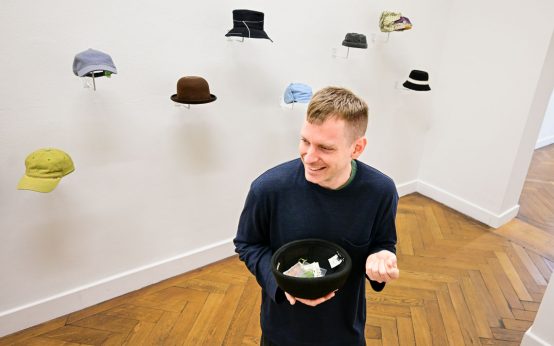 Martin La Roche und sein Musée Legitime, er nimmt die Kopfbedeckung ab und stellt die Ausstellungsstücke vor.