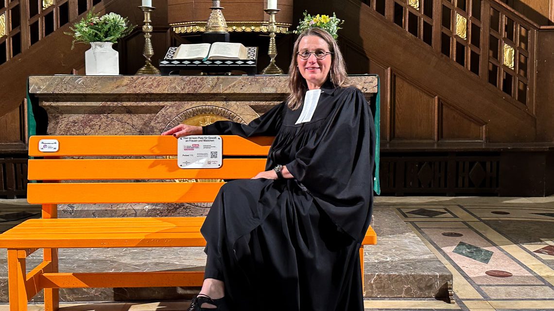 Für die Predigt hat Pfarrerin Ursula Kuhn die orangefarbene Bank vor den Altar gestellt: „Diese Bank schreit uns förmlich an: Schaut hin! Sprecht darüber! Nehmt die Geschichten ernst! Schweigen ist keine Option“, sagt sie im Gottesdienst.