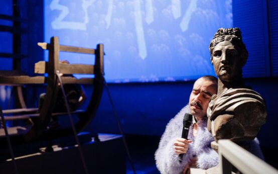 Der Museumswärter blickt auf das verwüstete „Troja“: Zwischen Götterköpfen und Pferdebauch herrscht Chaos – und niemand im Publikum will es gewesen sein