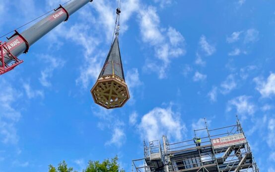 Ein Kran setzt die erneuerte Kirchturmspitze in Dotzheim millimetergenau auf das Dach der Evangelischen Kirche.