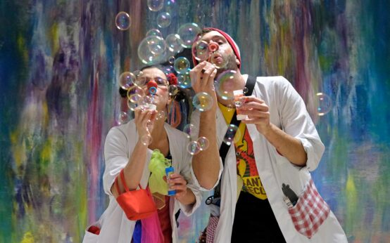 Zwei Clown mit roiter Nase pusten Seifenblasen.